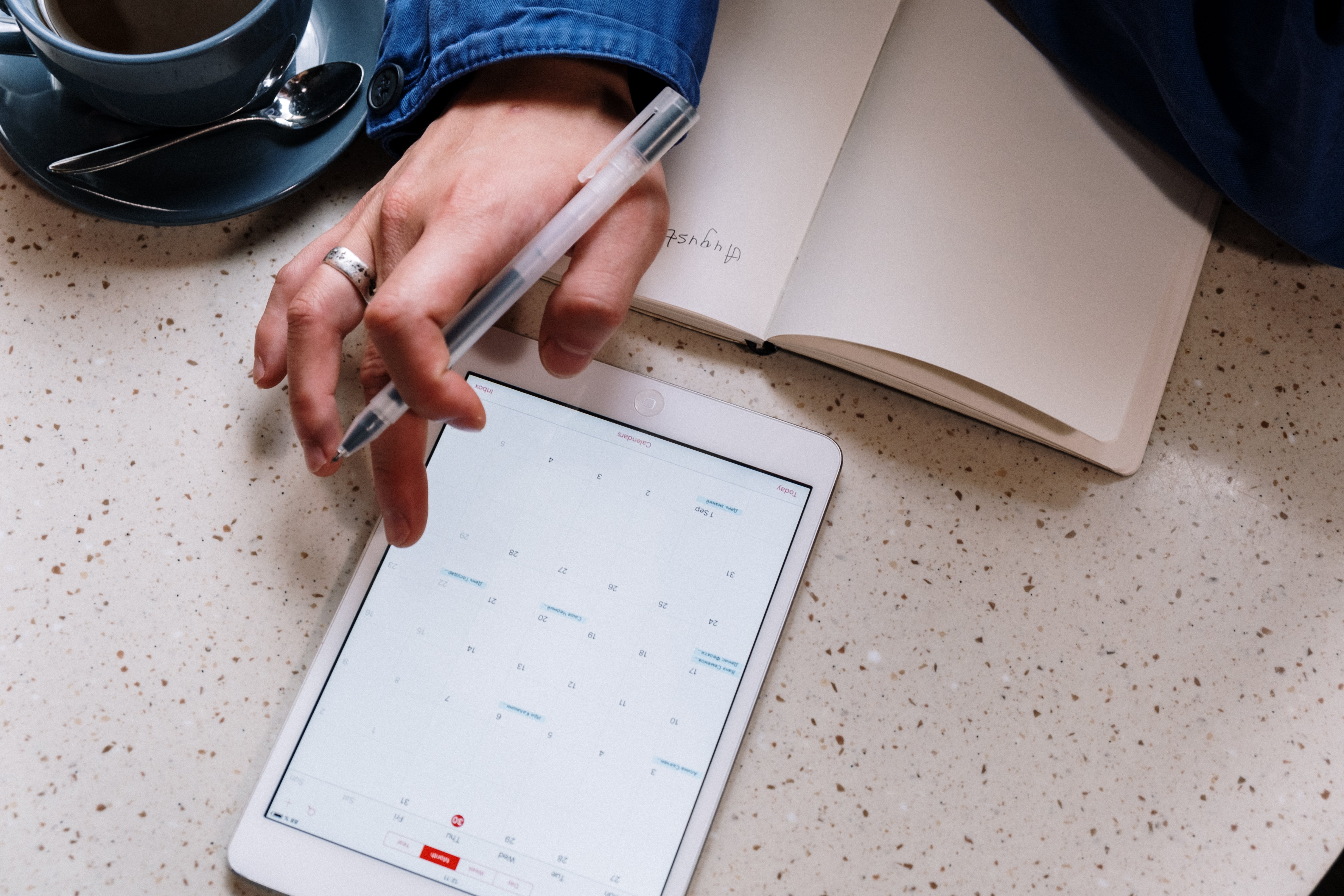 Calendar overview on tablet and person taking notes in notebook